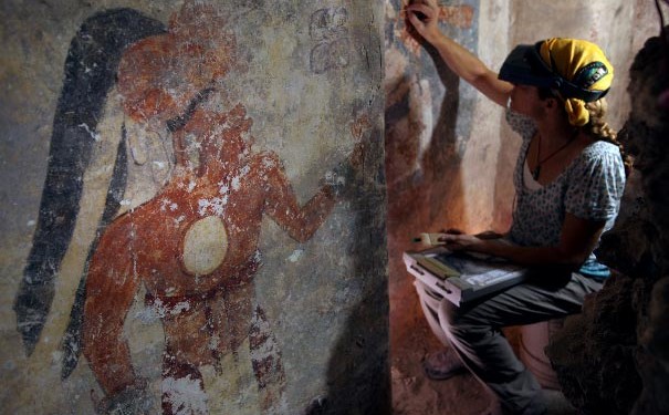 Conservator Angelyn Bass cleans and stabilises the surface of a wall of a Maya house that date to the 9th century. The figure of a man who may have been the town scribe appears on the wall to her left. Image: Tyrone Turner/2012 National Geographic